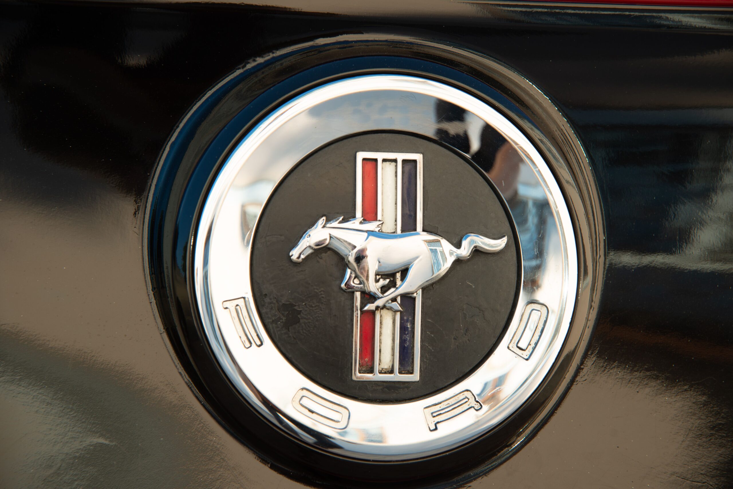 Detailed close-up of Ford Mustang emblem on a vehicle's black surface, symbolizing speed.